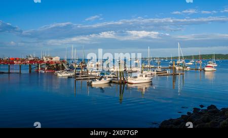 Bateaux à moteur et voiliers amarrés à Landings Marina dans le port de Rockland, Maine, États-Unis, sous un ciel bleu clair avec des nuages dispersés. Banque D'Images