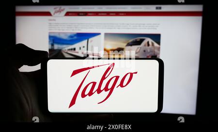 Personne tenant le téléphone portable avec le logo de la société espagnole de fabrication de train Talgo S.A. en face de la page Web de l'entreprise. Concentrez-vous sur l'affichage du téléphone. Banque D'Images