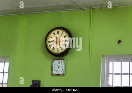 Ambewela, Sri Lanka - 28 janvier 2024 : horloges vintage et numériques sur un mur vert vibrant à la gare, faisant écho au charme historique. Banque D'Images