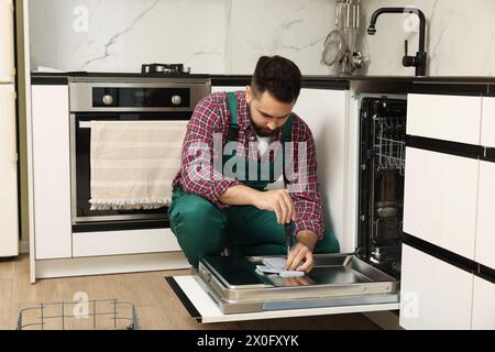 Réparateur lave-vaisselle réparateur avec tournevis dans la cuisine Banque D'Images