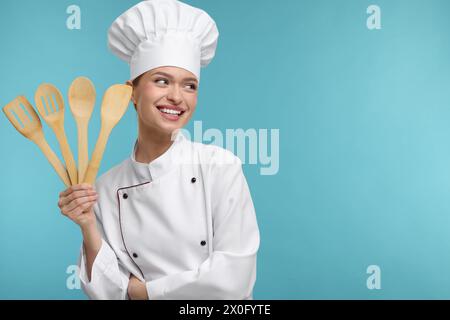 Femme heureuse chef en uniforme tenant des ustensiles en bois sur fond bleu clair, espace pour le texte Banque D'Images