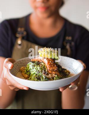 Une personne tient un bol de poke coloré rempli de nouilles vertes, une tranche de filet de saumon, et guacamole sur le dessus Banque D'Images