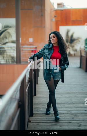 Femme élégante aux cheveux bouclés en tenue décontractée s'appuyant sur une balustrade au crépuscule Banque D'Images