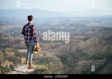 Femme dans une chemise à carreaux et un chapeau regardant le paysage d'en haut. Banque D'Images