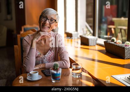 Femme mature est assise dans le café et relaxant. Banque D'Images