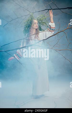 Une jeune femme dans une robe blanche se tient au milieu du brouillard dans une forêt mystique, exsudant un air de beauté éthérée et de mystère. Banque D'Images