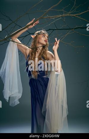 Une jeune femme dans une robe bleue ressemblant à une princesse elfe, tient délicatement une branche dans un cadre de studio. Banque D'Images