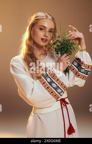Un jeune mavka dans une robe blanche tient délicatement une fleur dans un cadre de studio inspiré de la fée et de la fantaisie. Banque D'Images