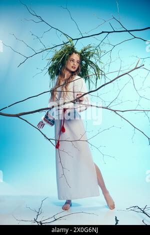 Un jeune mavka dans une robe blanche tient délicatement une branche d'arbre dans un cadre de studio fantastique. Banque D'Images