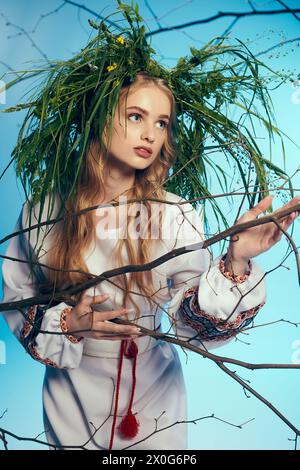 Un jeune mavka dans une robe blanche tient délicatement une branche feuillue dans un cadre de studio fantaisiste. Banque D'Images