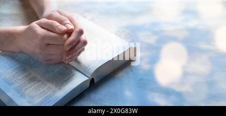 Religion. Femme chrétienne priant sur la Bible à table, gros plan. Effet bokeh. Conception de bannière Banque D'Images