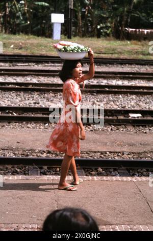 Une vendeuse transporte ses marchandises dans un bol sur sa tête sur la voie ferrée d'une gare à Java Ouest. [traduction automatique] Banque D'Images