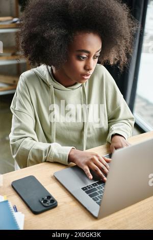 Une femme noire est assise à une table, intensément concentrée sur son ordinateur portable dans un espace de coworking moderne Banque D'Images