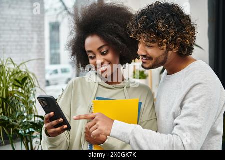 Un homme et une femme multiculturels plongés dans la visualisation de contenu sur un téléphone portable dans un espace de coworking moderne. Banque D'Images