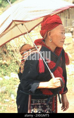 Une femme âgée du groupe ethnique ( également appelé ope) Hmong en costume traditionnel et avec parapluie portant un bébé sur son dos, sur la route entre Chiang Rai et Chiang Mai. Banque D'Images