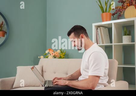 Souriant jeune homme caucasien travaillant en ligne sur ordinateur portable à la maison regardant la caméra Banque D'Images