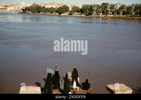 Des femmes égyptiennes en robes noires se lavant sur les rives de l'île du Nil de Roda. [traduction automatique] Banque D'Images