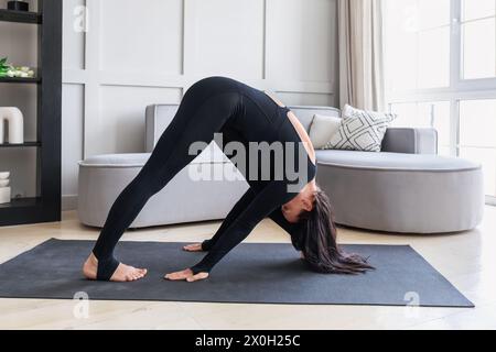 Une femme pratique le yoga à la maison, effectue une variation de l'exercice Parshvottanasana, pose d'extension latérale intense, et s'entraîne sur un tapis en sp noir Banque D'Images