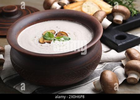 Délicieuse soupe de champignons maison dans un pot en céramique et ingrédients frais sur une table en bois Banque D'Images