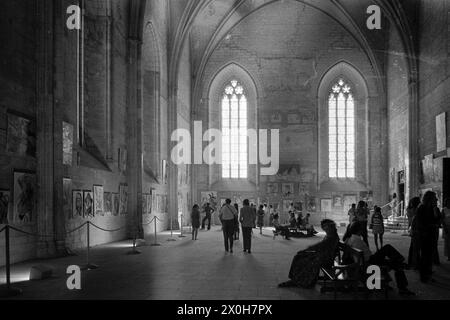 Vue dans une église. Une exposition de Piccasos se déroule à l'intérieur. Il y a de longs bancs au milieu. Les peintures sont accrochées aux murs. Certains des visiteurs sont assis sur les bancs, d'autres se promènent devant les tableaux. [traduction automatique] Banque D'Images