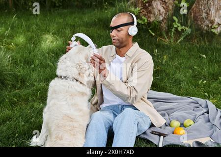 Homme afro-américain atteint de myasthénie grave assis sur une couverture, appréciant la musique avec chien Labrador portant des écouteurs. Banque D'Images