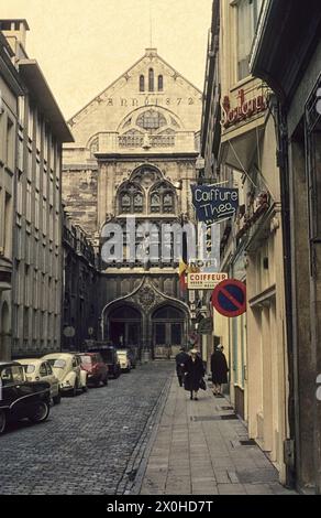 Une petite rue avec des voitures garées sur la gauche. Passants et vitrines de magasin sur la droite. Au bout de la rue, la vue extérieure des Handelsbeurs de 1872. [traduction automatique] Banque D'Images