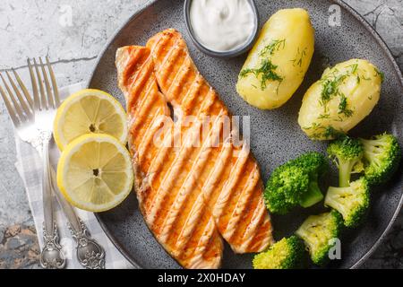 Saumon grillé, pommes de terre bouillies, brocoli et sauce à la crème dans une assiette sur la table. Vue horizontale de dessus Banque D'Images