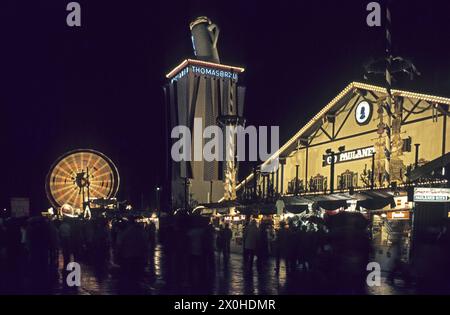 Les gens sur les stands devant la tente du festival Paulaner et une grande roue illuminée la nuit en arrière-plan à l'Oktoberfest de Munich. [traduction automatique] Banque D'Images