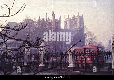 Vue à travers une clôture sur une rue et l'abbaye de Westminster. Un bus à impériale rouge typique circule le long de la route. [traduction automatique] Banque D'Images