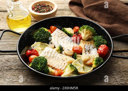 Morue savoureuse cuite avec des légumes dans une poêle à frire sur une table en bois Banque D'Images