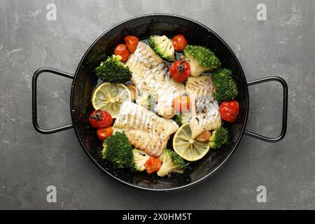 Morue savoureuse cuite avec des légumes dans une poêle à frire sur une table grise, vue de dessus Banque D'Images