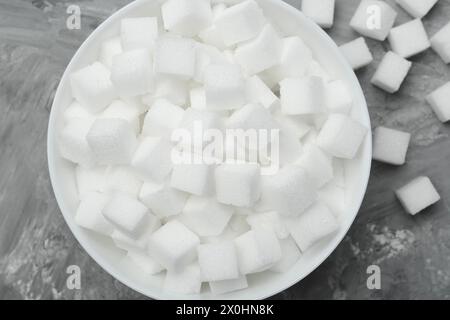 Cubes de sucre blanc dans un bol sur une table grise, vue de dessus Banque D'Images