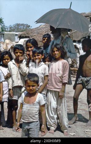 Un groupe d'enfants et un vieil homme posent pour une photo de groupe sur une place dans leur village. L'homme a une barbe blanche. Il tient un parapluie dans sa main pour se protéger du soleil. [traduction automatique] Banque D'Images