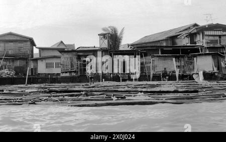 Vue sur la rive de la rivière Chao Phraya à Bangkok, Thaïlande, en juin 1972. Un homme est debout sur la banque. Derrière lui il y a des huttes en bois et des maisons en plusieurs rangées. Certains d'entre eux se tiennent sur des pilotis. [traduction automatique] Banque D'Images