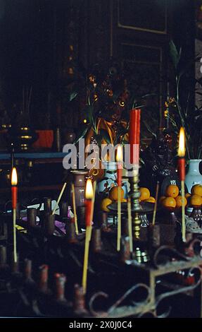 Un sanctuaire avec des offrandes à Singapour. Au premier plan brûlant des bougies et des bâtons d'encens. Les oranges, entre autres, étaient offertes comme offrandes. Sur la droite entre deux vases une statue de Bouddha. [traduction automatique] Banque D'Images