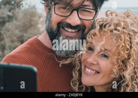 Un jeune couple adulte heureux, amoureux de la photographie de selfie en plein air. Homme et femme joyeux effectuant un appel vidéo. Les personnes mûres aiment l'amour et la relation dans les activités de loisirs. Cheveux bouclés et barbe Banque D'Images