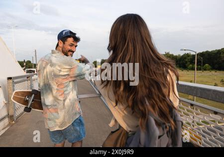 Jeune hipster élégant couple vintage skateboarders marchant dans la rue tenant des longboards après avoir patiné sur le pont. Homme et femme jeunesse culture avec Banque D'Images