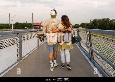 Jeune hipster élégant couple vintage skateboarders marchant dans la rue tenant des longboards après avoir patiné sur le pont. Homme et femme jeunesse culture avec Banque D'Images