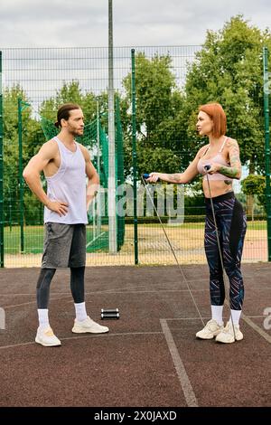Une femme en vêtements de sport et son entraîneur personnel, se tiennent debout sur un court de tennis, déterminés et motivés à faire de l'exercice ensemble. Banque D'Images