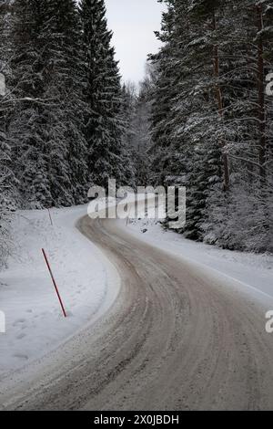 Paysage hivernal enneigé, une route à travers une forêt de pins et d'épicéas enneigés en Suède Banque D'Images