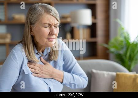 Femme mature éprouvant de l'inconfort et tenant sa poitrine en raison de la douleur. Elle semble anxieuse et inquiète, indiquant peut-être un problème de santé. Banque D'Images