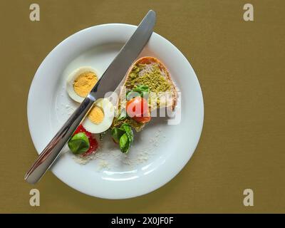 Une tranche de pain à tartiner au pesto, oeuf tranché, tomate, basilic et couteau sur une assiette blanche, petit déjeuner, Allemagne Banque D'Images