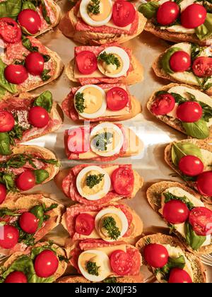 Tranches de pain au salami, œufs tranchés, tomates, mozzarella, persil, feuilles de basilic, tartinade au pesto vert Banque D'Images