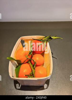 Les fruits oranges de la clémentine ou des mandarines emballés dans une boîte avec des feuilles pour la consommation Banque D'Images