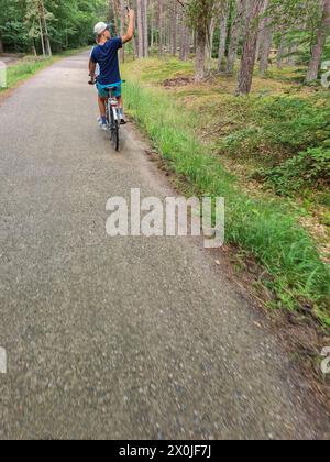 Deux adolescents en tandem sur une route étroite à travers une forêt verdoyante dans la station de vacances de Prerow, Fischland Darß, Mecklembourg-Poméranie occidentale, Allemagne Banque D'Images