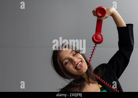 Jeune femme latino-américaine avec un casque rouge et une attitude positive, pose avec des gestes amusants. Concept de technologie jeune et vintage Banque D'Images