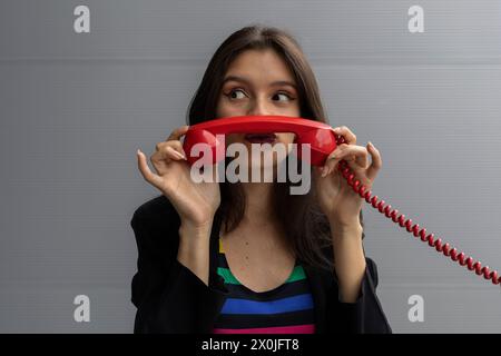 Jeune femme latino-américaine avec un casque rouge et une attitude positive, pose avec des gestes amusants. Concept de technologie jeune et vintage Banque D'Images