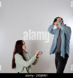 Femme à genoux proposant le mariage à son petit ami avec une boîte à anneaux dans ses mains et il est surpris Banque D'Images