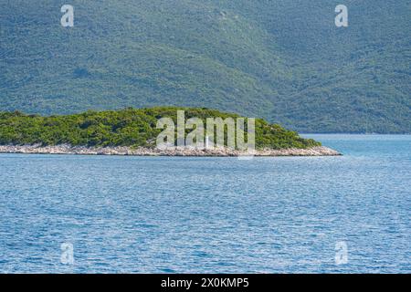 Une petite île rectangulaire se trouve au milieu d'un vaste lac, entourée d'eau et de paysages herbeux. L'horizon est parsemé de côtes et d'océani Banque D'Images