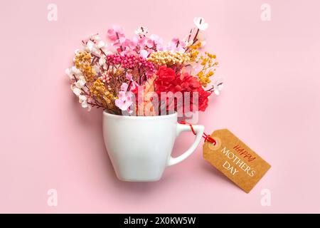 Bonne fête des mères. Tasse blanche de café avec diverses fleurs et étiquette de vente brune avec le texte Happy Mothers Day sur fond rose Banque D'Images